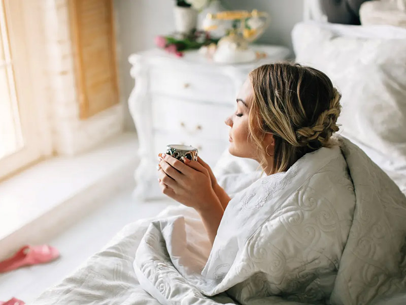 a woman drinking something on her bed