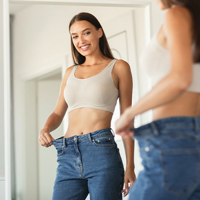 Woman smiling at her figure while pulling loose pants